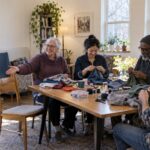 Neighbors working together on fabric repairs around a shared table in a bright community room.