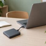 An open laptop and portable storage drive on a clean home office desk.